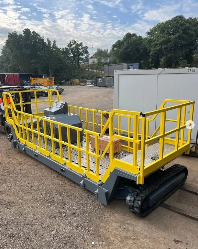 A heavy-duty mobile tunnel platform with rubber tracks, a non-slip metal deck, an integrated control console, and safety-yellow guard rails; used for railway traversal.